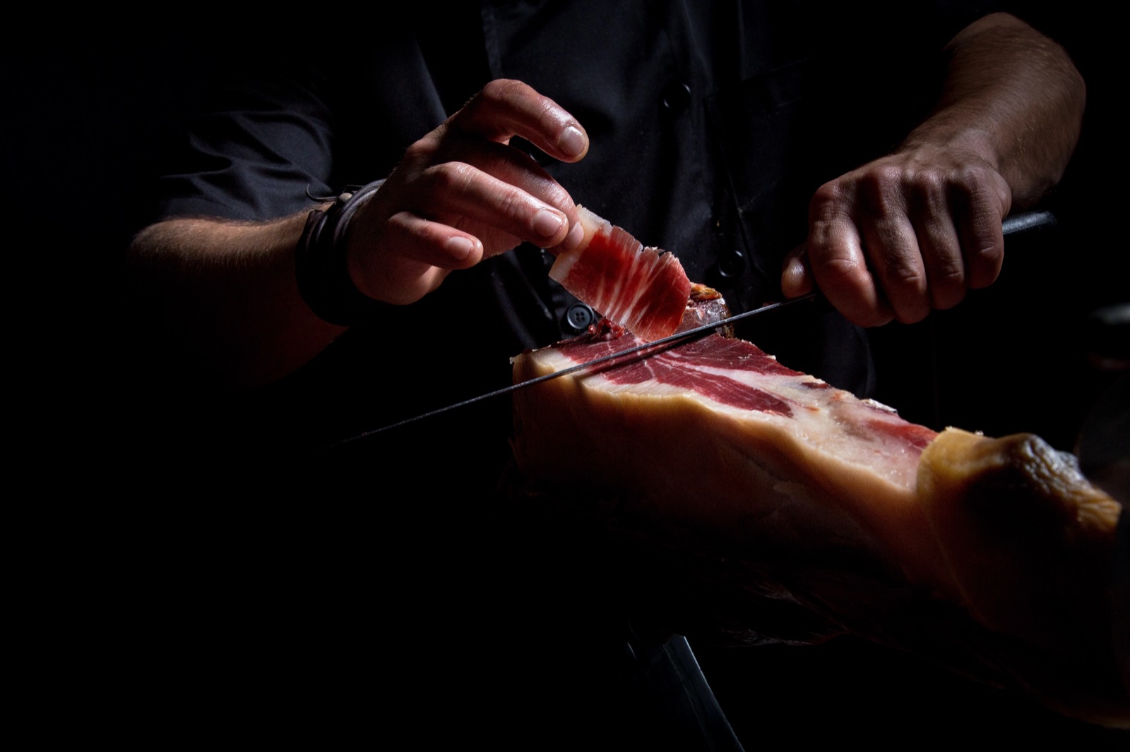 Manos cortando jamón ibérico a cuchillo en penumbra