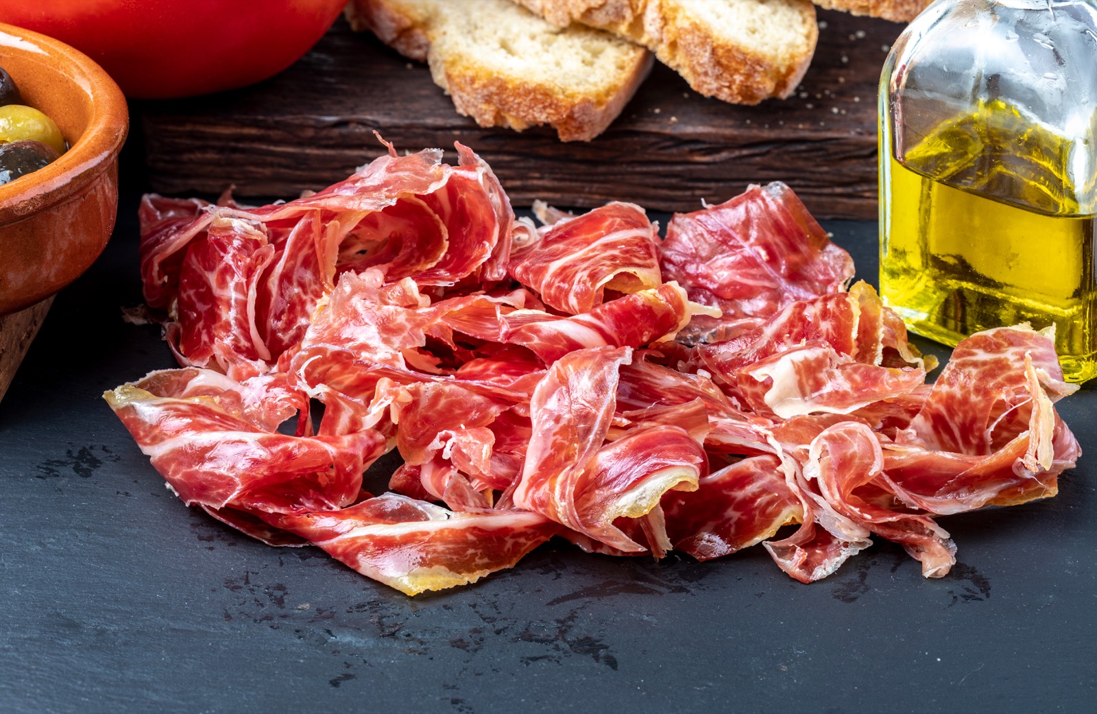 Lonchas de jamón ibérico sobre pizarra con aceite de oliva y pan