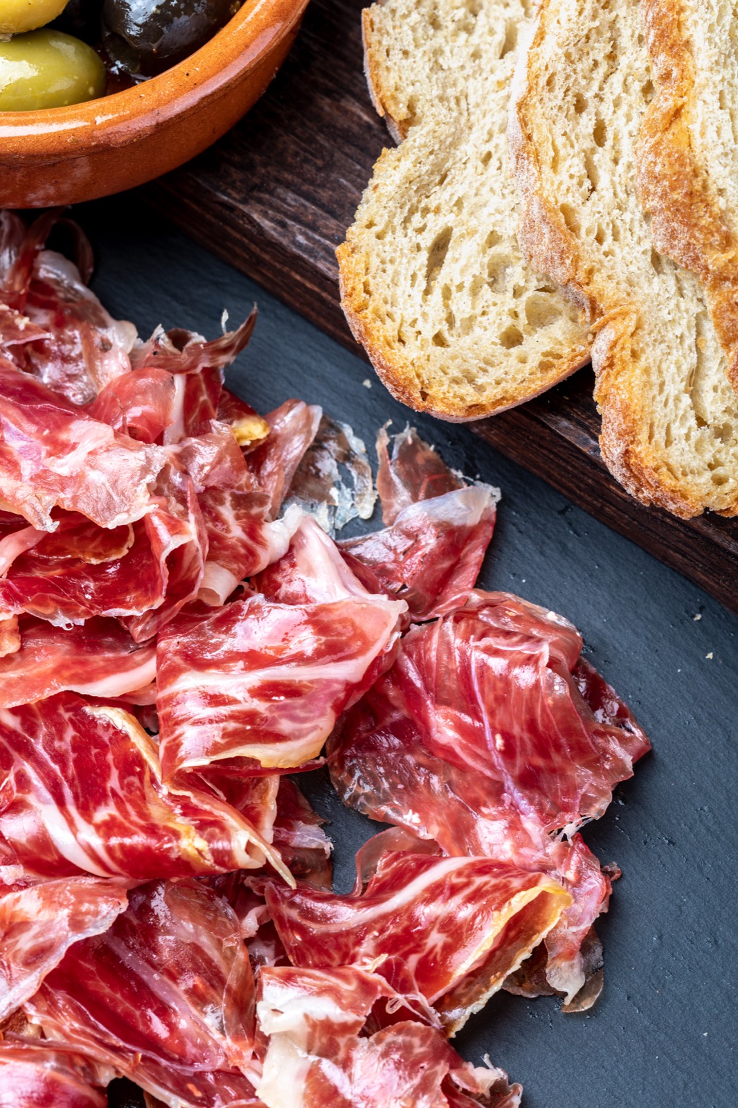 Lonchas de jamón ibérico sobre pizarra con pan rústico